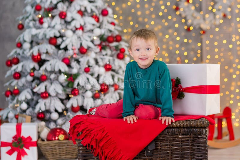 Ragazzo del bambino della famiglia di Natale che posa sulla scatola di legno vicino ai presente ed all'albero operato bianco del fotografia stock Ragazzo del bambino della famiglia di Natale che posa sulla scatola di legno vicino ai presente ed all'albero operato bianco del fotografia stock