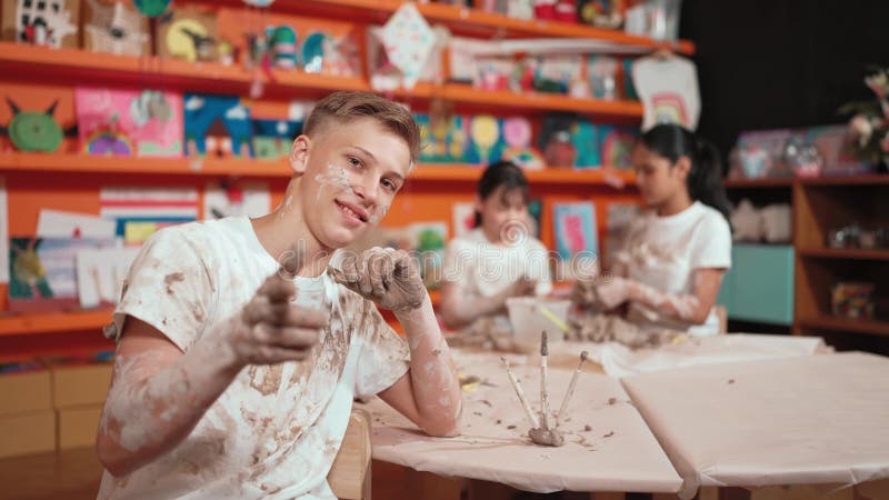 Ragazzo della scuola superiore che guarda la macchina fotografica mentre i bambini modellano l'argilla. costruzione