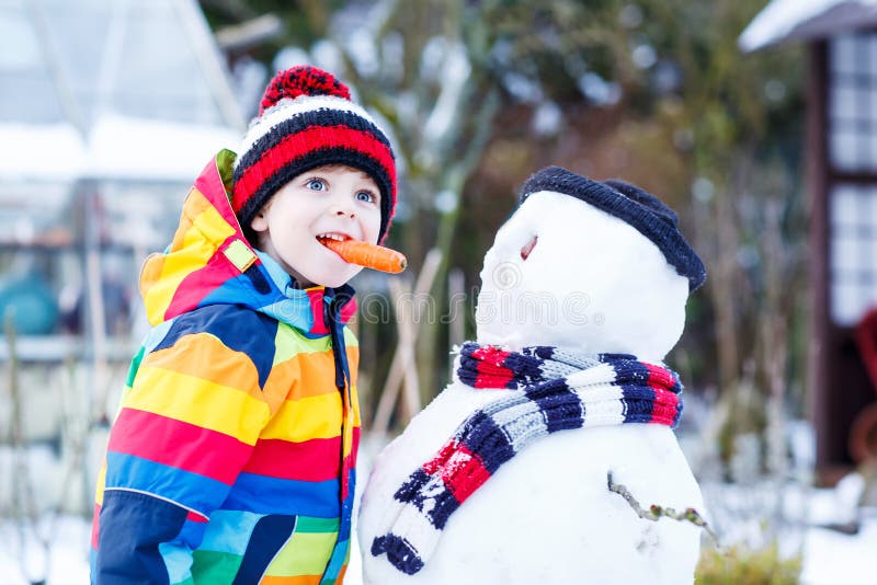 Ragazzo divertente del bambino in vestiti variopinti che fanno un pupazzo di neve, all'aperto fotografia stock libera da diritti Ragazzo divertente del bambino in vestiti variopinti che fanno un pupazzo di neve, all'aperto fotografia stock libera da diritti
