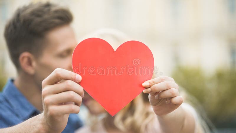 Ragazzo ed amica che stringono a sé e che si nascondono dietro il cuore di carta, amore romantico fotografie stock Ragazzo ed amica che stringono a sé e che si nascondono dietro il cuore di carta, amore romantico fotografie stock