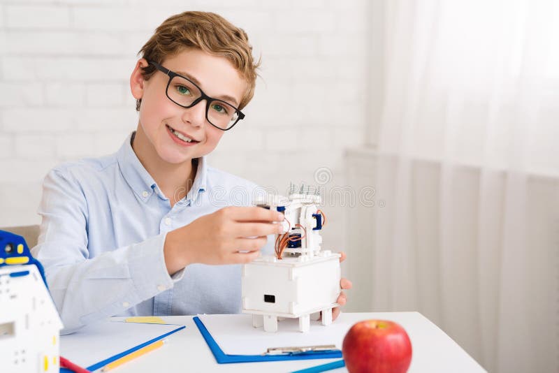 Ragazzo felice che costruisce robot elettrico e che esamina macchina fotografica fotografia stock libera da diritti Ragazzo felice che costruisce robot elettrico e che esamina macchina fotografica fotografia stock libera da diritti