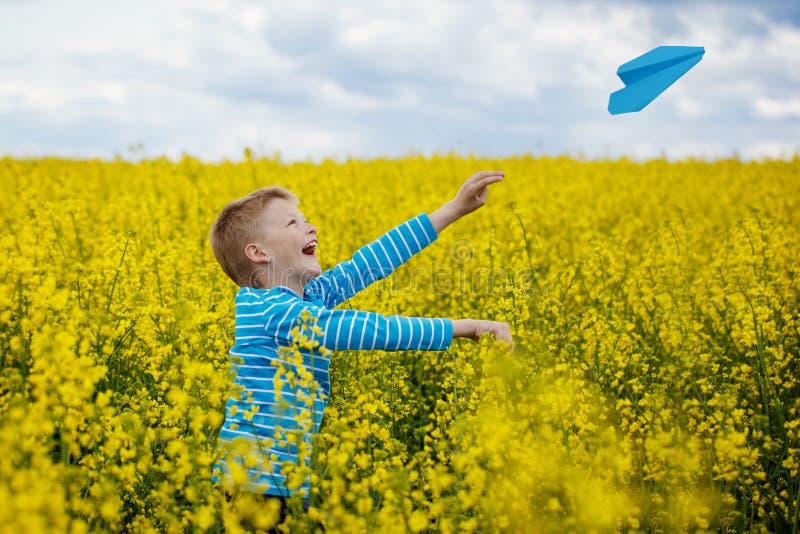Ragazzo felice che pende e che getta aeroplano di carta blu sul sole luminoso fotografia stock libera da diritti Ragazzo felice che pende e che getta aeroplano di carta blu sul sole luminoso fotografia stock libera da diritti