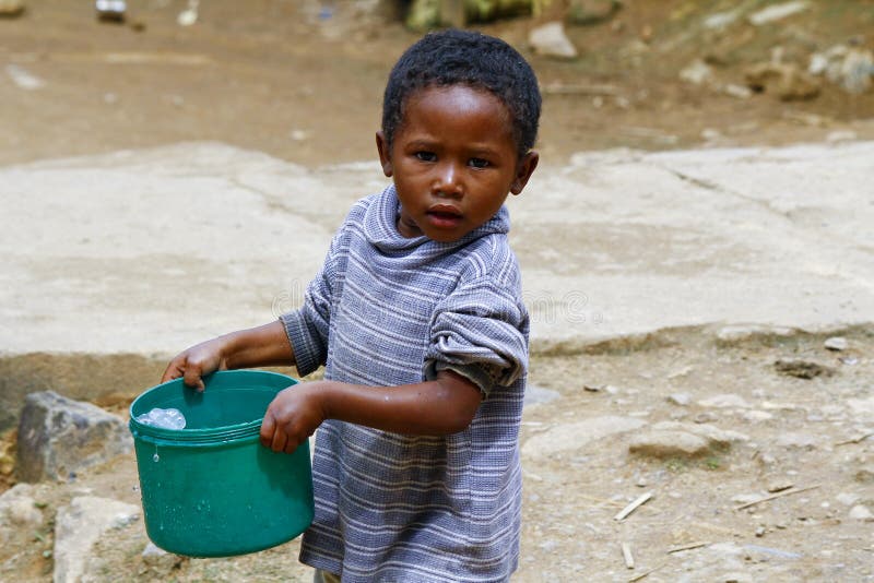 Ragazzo malgascio povero che porta il secchio di acqua di plastica