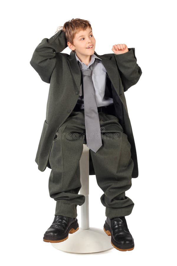 Ragazzo nel vestito del grande uomo che si siede sulla presidenza isolata immagini stock libere da diritti Ragazzo nel vestito del grande uomo che si siede sulla presidenza isolata immagini stock libere da diritti