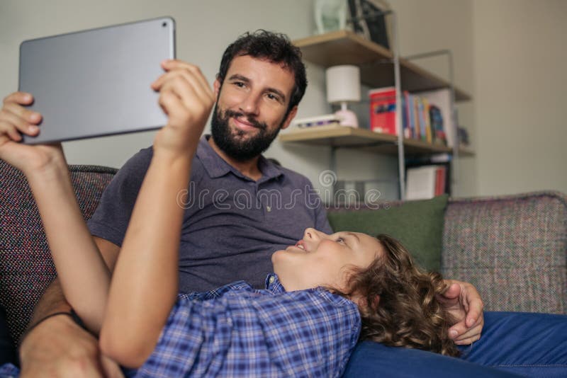 Ragazzo sorridente ed suo padre facendo uso di una compressa a casa fotografia stock libera da diritti Ragazzo sorridente ed suo padre facendo uso di una compressa a casa fotografia stock libera da diritti