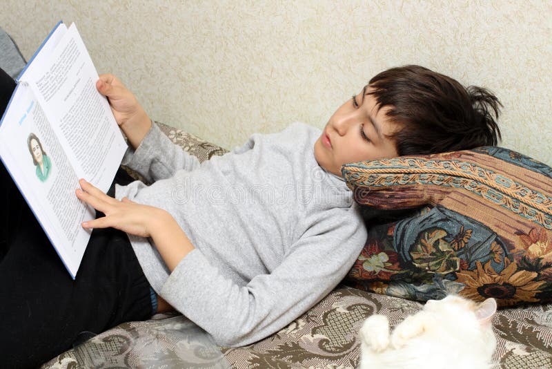 Ragazzo sulla base con il gatto, libro di lettura immagine stock libera da diritti Ragazzo sulla base con il gatto, libro di lettura immagine stock libera da diritti
