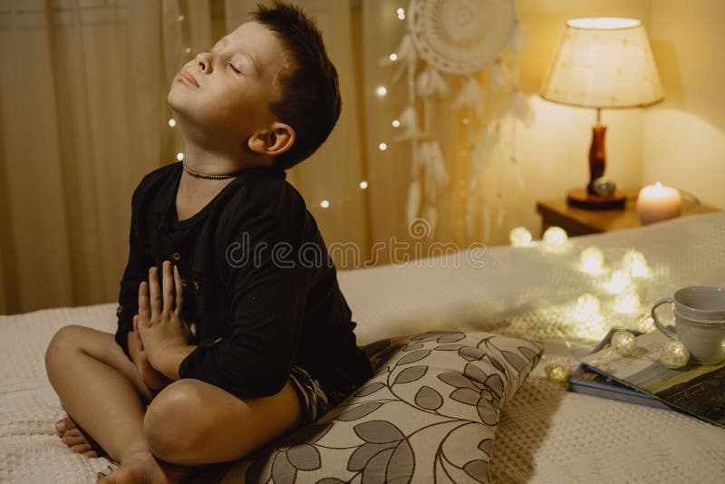 Ragazzo sveglio che prega per il regalo con gli occhi chiusi nella sala o di sera fotografia stock libera da diritti Ragazzo sveglio che prega per il regalo con gli occhi chiusi nella sala o di sera fotografia stock libera da diritti