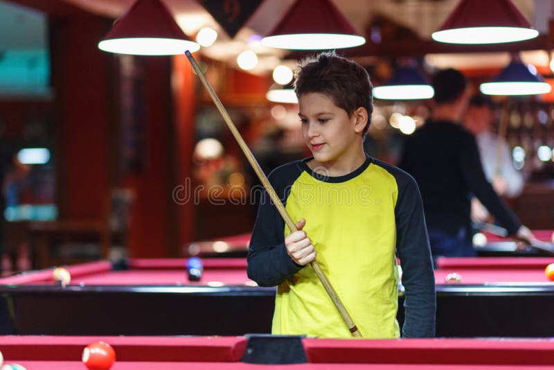 Ragazzo sveglio nel biliardo giallo dei giochi della maglietta o stagno in club Il ragazzino impara giocare lo snooker Ragazzo co immagine stock libera da diritti Ragazzo sveglio nel biliardo giallo dei giochi della maglietta o stagno in club Il ragazzino impara giocare lo snooker Ragazzo co immagine stock libera da diritti