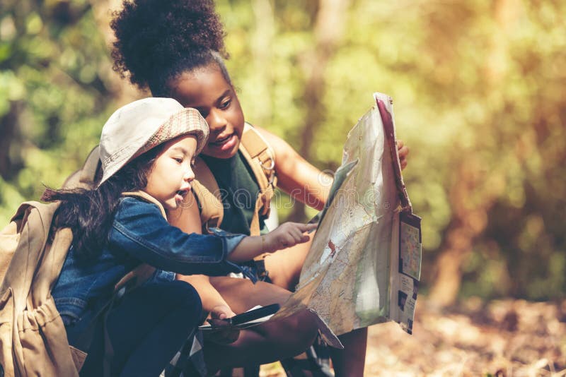 Raggruppamento di bambini che controllano la mappa per esplorare e trovare le direzioni nella giungla di camping natura e avventu