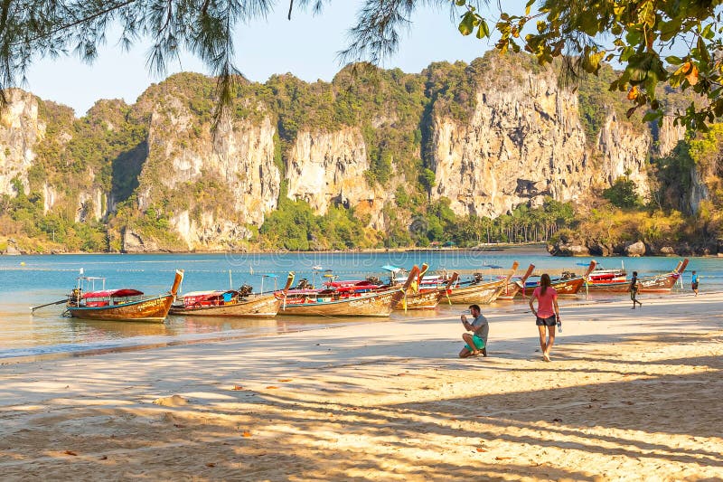 Railay Thailand - Februari 19, 2019: En man fotograferar fartyget på stranden som huka sig ned på ett knä Bred sandig tropisk str royaltyfri foto Railay Thailand - Februari 19, 2019: En man fotograferar fartyget på stranden som huka sig ned på ett knä Bred sandig tropisk str royaltyfri foto