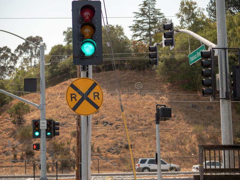 Railroad crossing sign on a track intersection on a busy street with hill