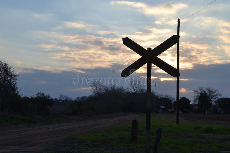 Railroad signal in contrast to sunset and darkening of a semi-cloudy sky and a country street stock photo Railroad signal in contrast to sunset and darkening of a semi-cloudy sky and a country street stock photo