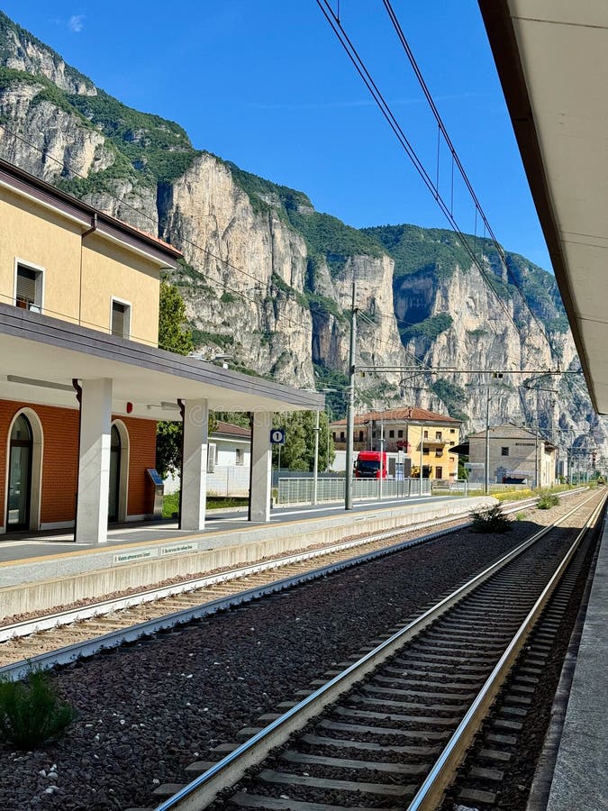 Railway Station Platform with Dramatic Alpine Cliffs and Electric Train Tracks royalty free stock photography