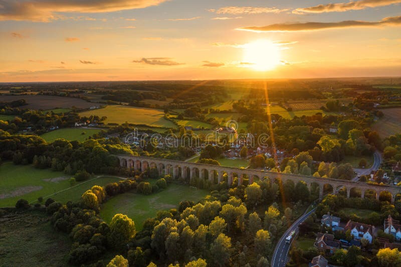 The railway viaduct at Chappel and Wakes Colne in Essex, England the sun a gold ball just above the horizon casting rays light and