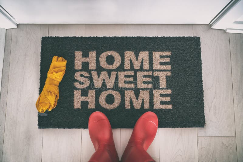 Rain boots selfie walking on doormat entrance welcome sign saying Home Sweet Home with yellow umbrella for autumn real estate