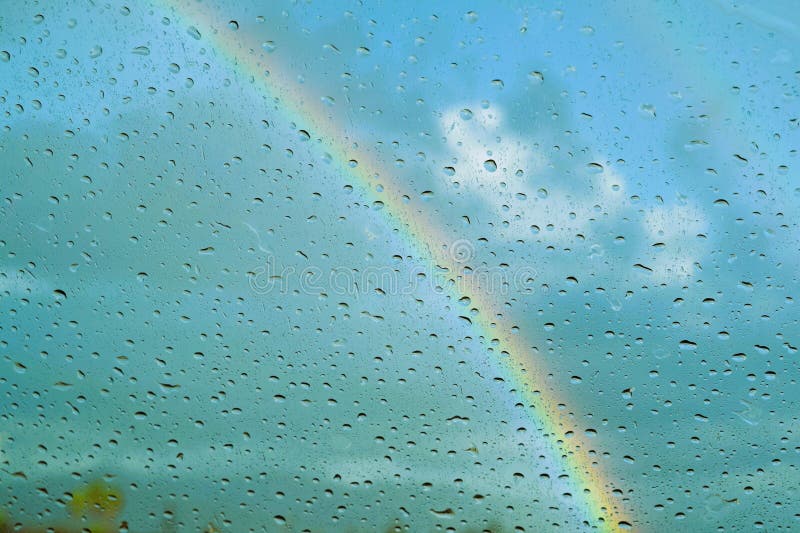 Parbrizul acoperit cu ploaie împotriva curcubeului. Raiinbow privit printr-un parbriz stropit de ploaie luminează o zi de călătorie cu mașina