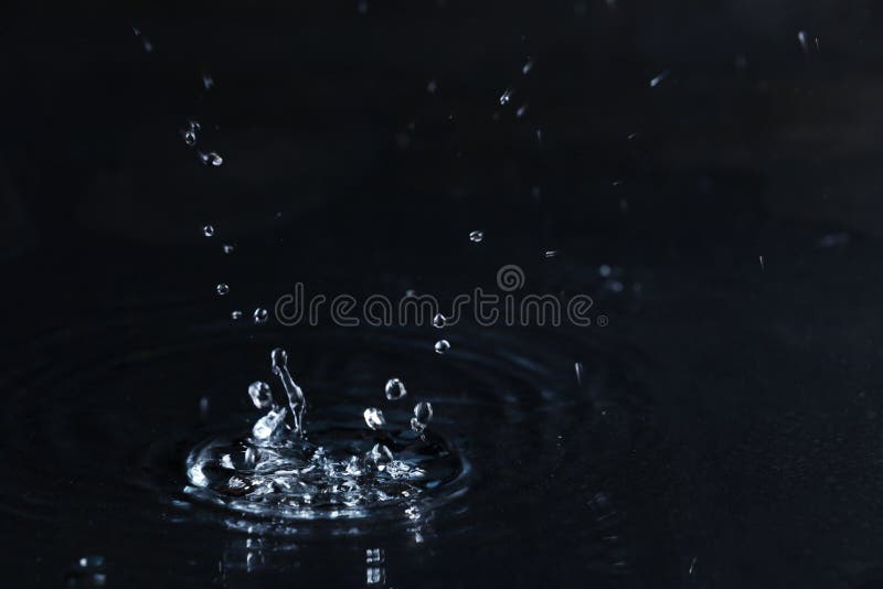 Rain drop falling down into puddle on dark