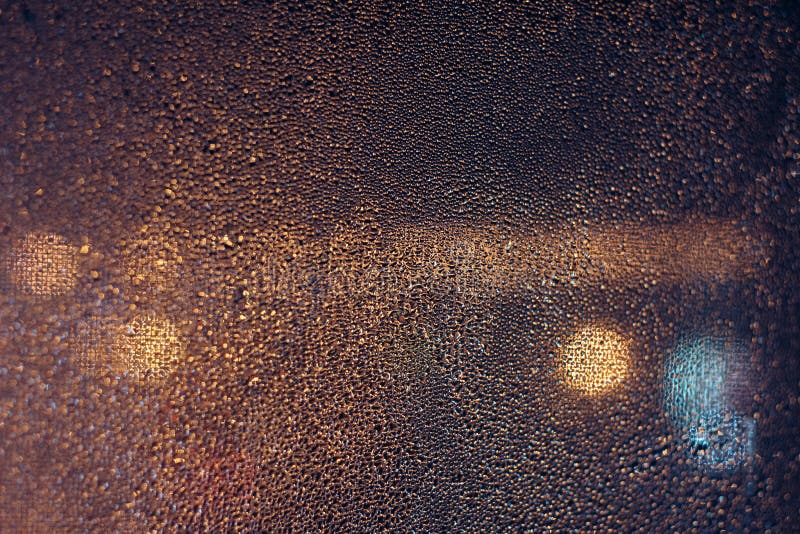 Rain drops on window with road light bokeh, City life in night in rainy season abstract background, water drop on the glass, night