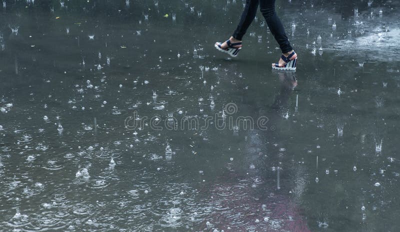 rain on the pavement and a woman walking along a puddle