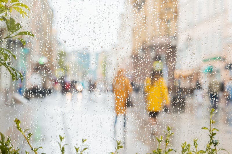 Rain on a window, looking out to people in a street scene. Silhouettes of girls in bright beautiful yellow coats