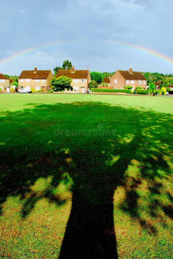 Lunga ombra di un albero con arcobaleno sul case, dopo che la pioggia è caduta.