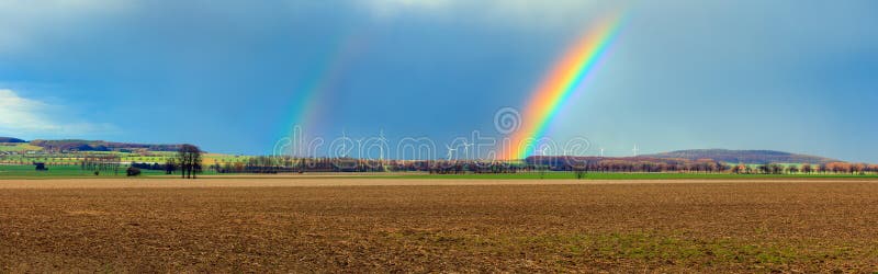 Rainbow over a plowed field with village in background, Germany. panoramic view