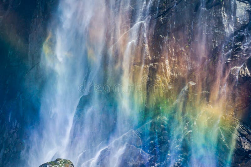Rainbow shining in the mist of a waterfall against black rocks. Rainbow shining in the mist of a waterfall against black rocks.
