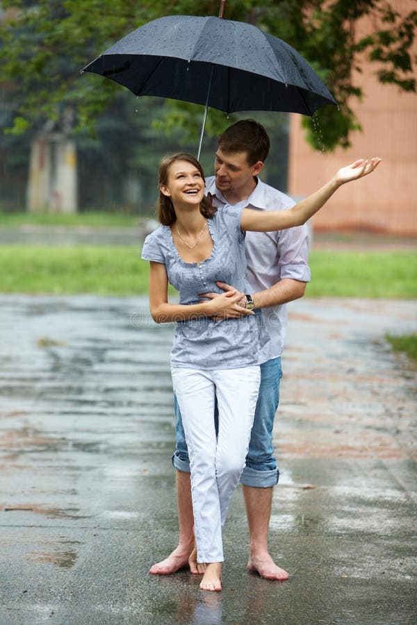A young couple walking in the rain barefoot stock image.