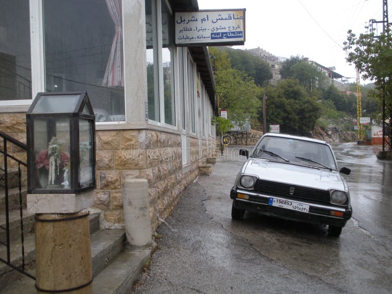 A rainy day on the main street of a Lebanese village. A typical Christian shrine is placed at the foot of the stairs next to a restaurant, near the road. A rainy day on the main street of a Lebanese village. A typical Christian shrine is placed at the foot of the stairs next to a restaurant, near the road.