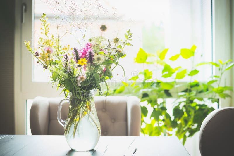 Ramo de flores en un florero de cristal en la tabla delante de una ventana con una silla Decoración casera fotos de archivo Ramo de flores en un florero de cristal en la tabla delante de una ventana con una silla Decoración casera fotos de archivo