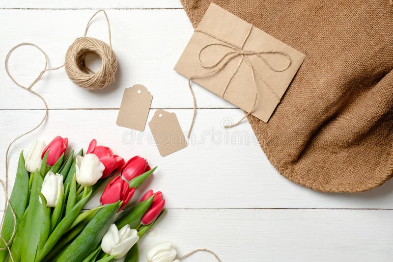 Ramo de flores de los tulipanes, sobre de Kraft, guita, etiquetas, arpillera en la tabla de madera blanca Tarjeta de felicitación fotografía de archivo libre de regalías Ramo de flores de los tulipanes, sobre de Kraft, guita, etiquetas, arpillera en la tabla de madera blanca Tarjeta de felicitación fotografía de archivo libre de regalías