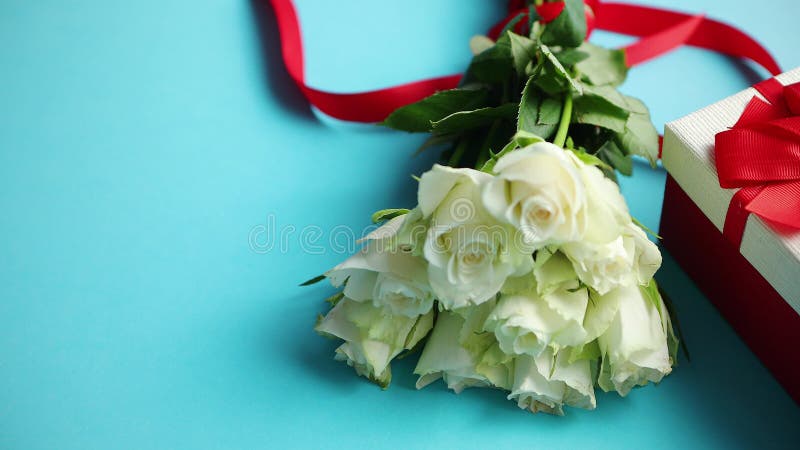 Ramo de rosas blancas con el arco rojo en fondo azul Regalo encajonado en lado