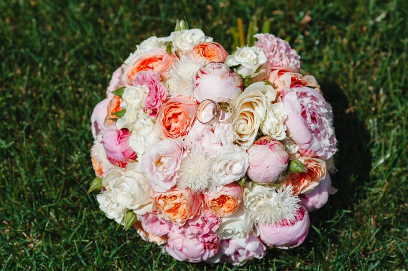 Ramo hermoso de flores que mienten en la hierba verde con los anillos de bodas del oro fotos de archivo libres de regalías Ramo hermoso de flores que mienten en la hierba verde con los anillos de bodas del oro fotos de archivo libres de regalías