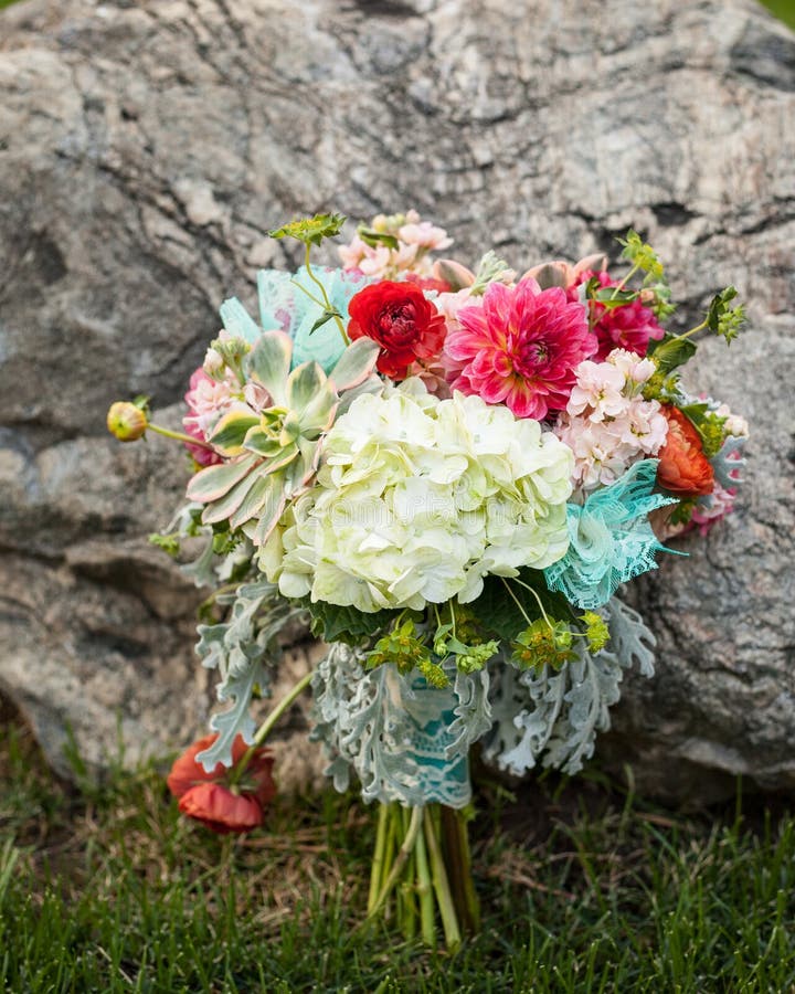 Ramo nupcial brillante y hermoso de flores que se sientan en la hierba y que se inclinan contra una roca fotos de archivo Ramo nupcial brillante y hermoso de flores que se sientan en la hierba y que se inclinan contra una roca fotos de archivo