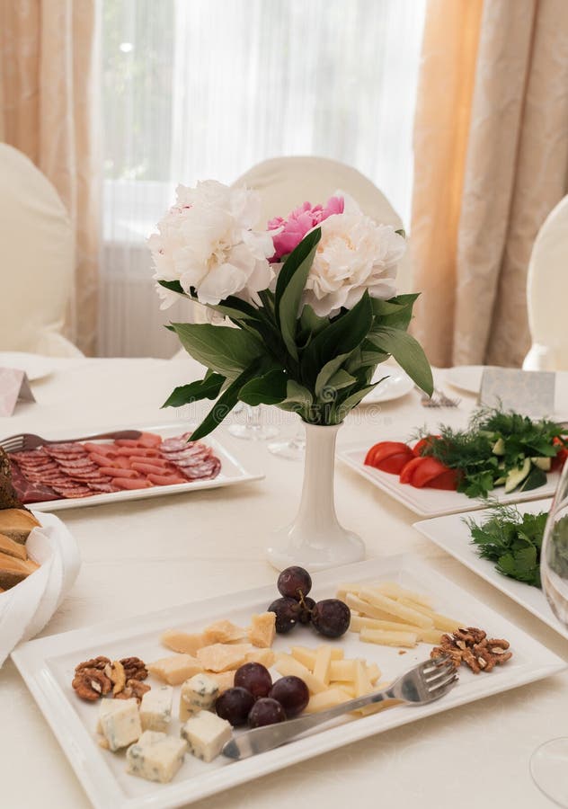 Ramo que se casa hermoso de peonías blancas y rosadas en el florero blanco en la tabla de cena en la falta de definición Ajuste d fotografía de archivo libre de regalías Ramo que se casa hermoso de peonías blancas y rosadas en el florero blanco en la tabla de cena en la falta de definición Ajuste d fotografía de archivo libre de regalías