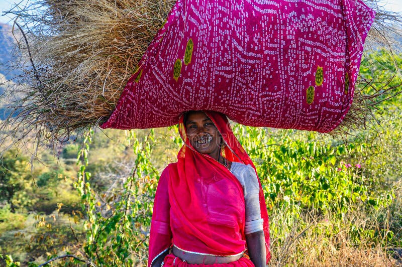 Ranakpur, India - Jan 02, 2020: Indian woman carries hay on her head. Ranakpur, India - Jan 02, 2020: Indian woman carries hay on her head