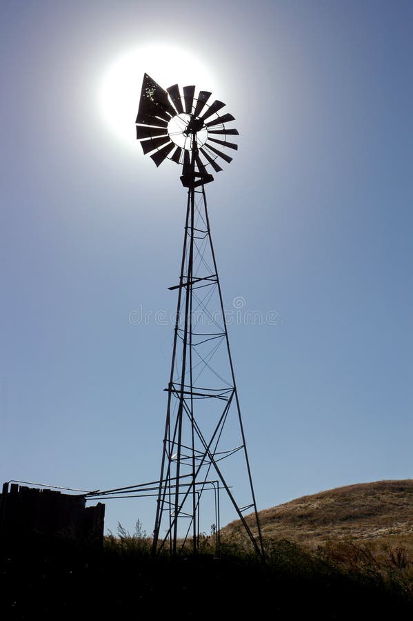 Bullet Ridden Ranch Windmill Silhouette with Blazing Sun Behind. Bullet Ridden Ranch Windmill Silhouette with Blazing Sun Behind