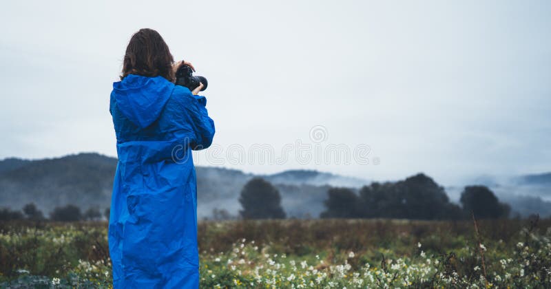 Rapariga turística fotógrafa na capa de chuva azul segura em mãos femininas fotocâmera fotográfica fotografar montanha sapateira, fotografia de stock royalty free Rapariga turística fotógrafa na capa de chuva azul segura em mãos femininas fotocâmera fotográfica fotografar montanha sapateira, fotografia de stock royalty free