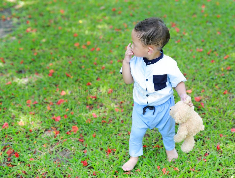 Rapaz pequeno asiático adorável que anda com o urso de peluche no jardim exterior fotos de stock Rapaz pequeno asiático adorável que anda com o urso de peluche no jardim exterior fotos de stock