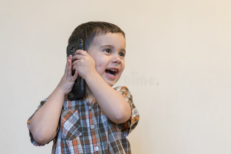 Rapaz pequeno bonito que fala pelo telefone celular no fundo claro Posi??o feliz do rapaz pequeno e fala no smartphone em casa imagens de stock royalty free Rapaz pequeno bonito que fala pelo telefone celular no fundo claro Posi??o feliz do rapaz pequeno e fala no smartphone em casa imagens de stock royalty free