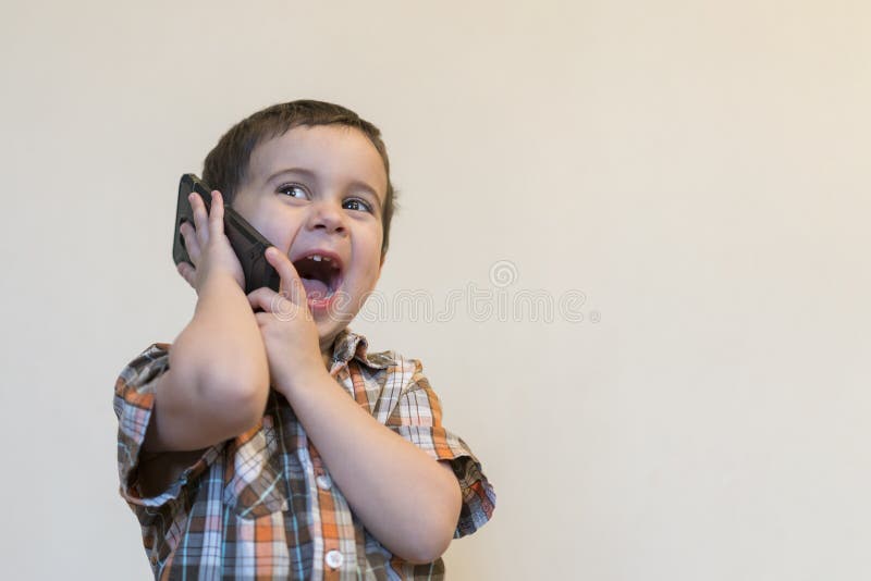 Rapaz pequeno bonito que fala pelo telefone celular no fundo claro Posi??o feliz do rapaz pequeno e fala no smartphone em casa foto de stock royalty free Rapaz pequeno bonito que fala pelo telefone celular no fundo claro Posi??o feliz do rapaz pequeno e fala no smartphone em casa foto de stock royalty free