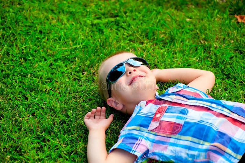 Rapaz pequeno feliz que encontra-se para baixo descansando na grama verde foto de stock Rapaz pequeno feliz que encontra-se para baixo descansando na grama verde foto de stock