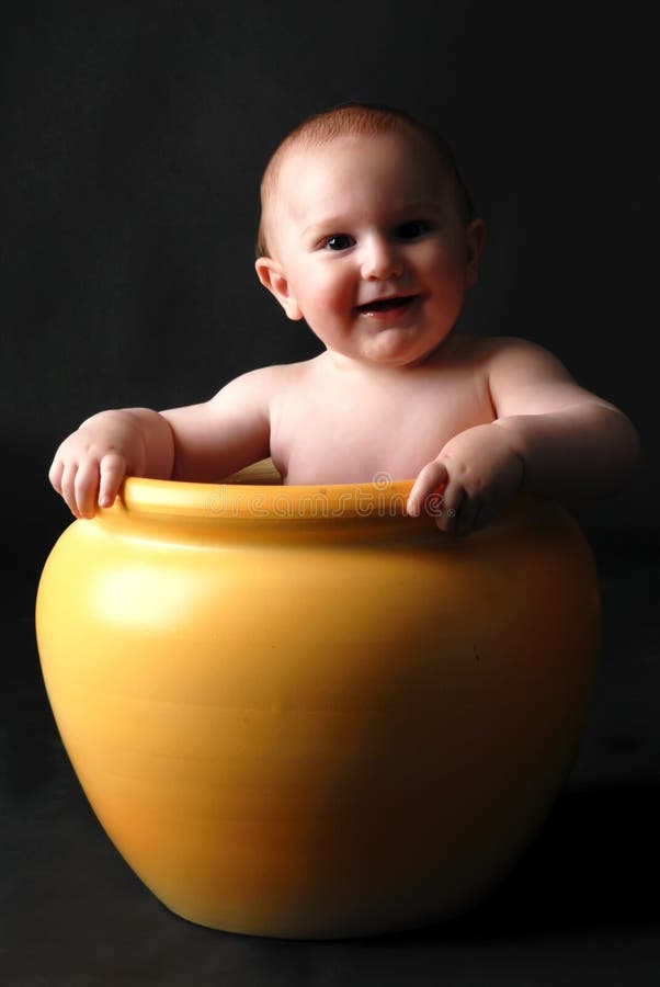 Little boy sitting inside of a large yellow planter pot isolated against a black background. Little boy sitting inside of a large yellow planter pot isolated against a black background.