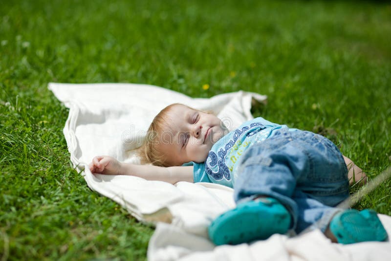 Rapaz pequeno que dorme em uma grama no verão fotografia de stock Rapaz pequeno que dorme em uma grama no verão fotografia de stock