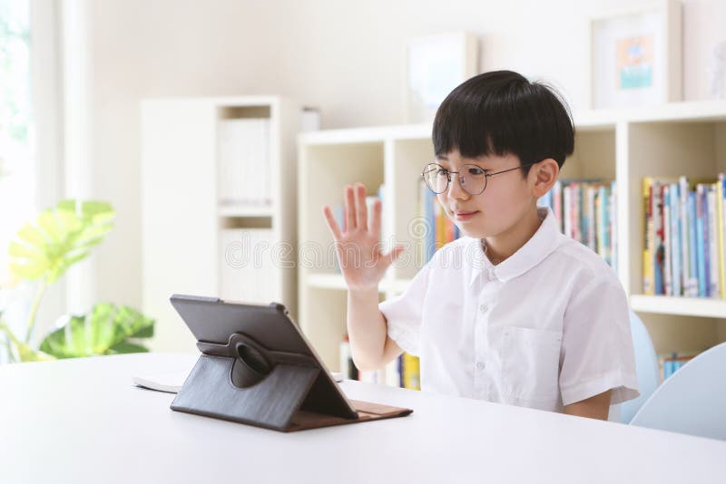 Boy studying via internet online with laptop and tablet, greeting teacher and friends, taking network video lessons at home. Boy studying via internet online with laptop and tablet, greeting teacher and friends, taking network video lessons at home