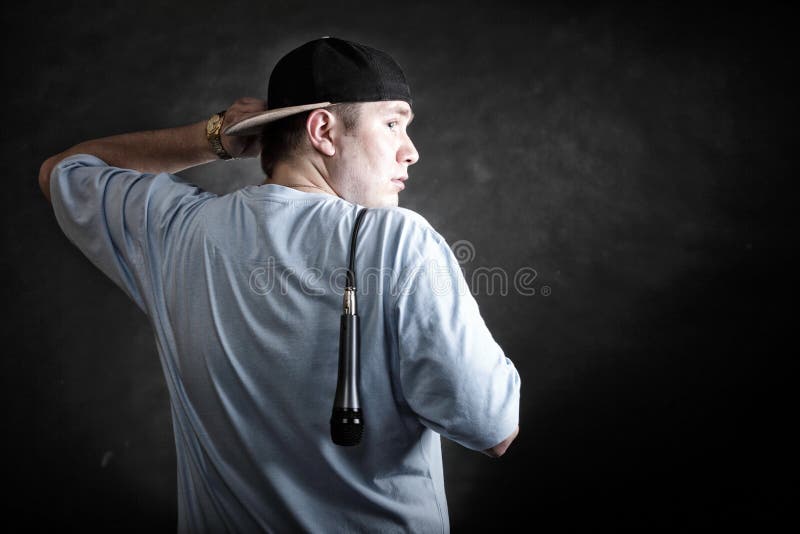 Rapper attitude rap singer hip Hop Dancer performing. Young man with cap microphone back view black grunge background. Rapper attitude rap singer hip Hop Dancer performing. Young man with cap microphone back view black grunge background