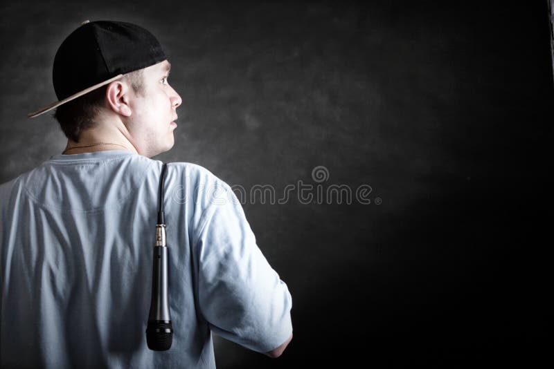 Rapper attitude rap singer hip Hop Dancer performing. Young man with cap microphone back view black grunge background. Rapper attitude rap singer hip Hop Dancer performing. Young man with cap microphone back view black grunge background