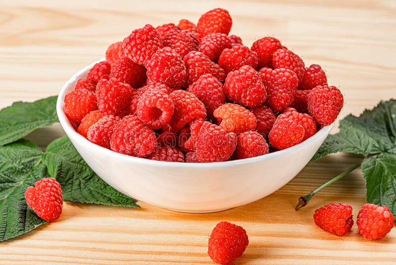 Raspberries on white plate on wooden table with leaves. Organic raspberries grown without use of chemical fertilizers and