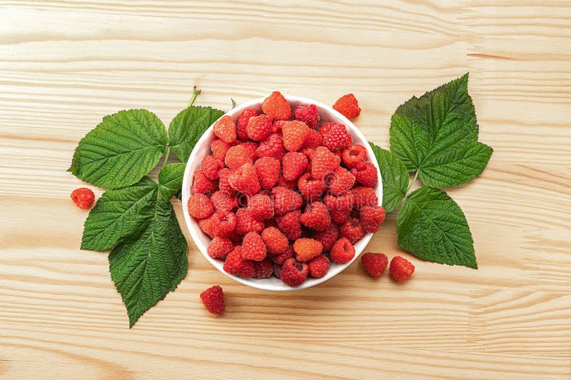 Raspberries on white plate on wooden table with leaves. Organic raspberries grown without use of chemical fertilizers and