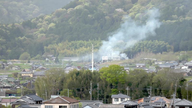 Rauch steigt aus dem Brand in der kleinen japanischen Stadt zu Füßen des grünen Berges